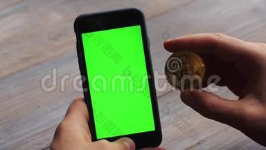 人使用垂直智能手机与绿色屏幕。 男子`手拿手机和一枚金币的特写镜头
